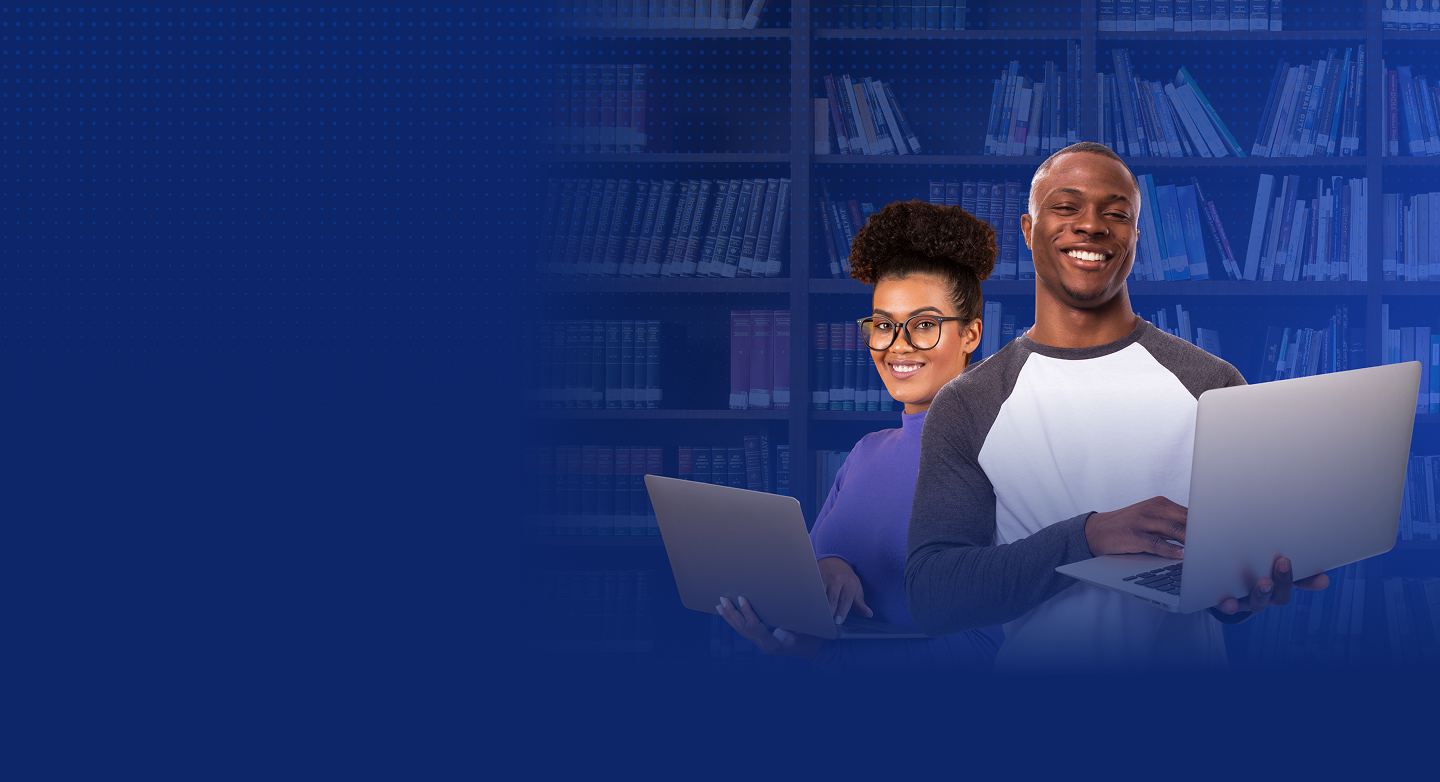 Two smiling students holding laptops in front of library shelves